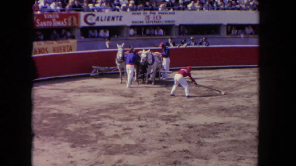 Workers maintain the dirt ring at a 1962 Los Angeles racetrack, with horses grouped near the barrier and spectators above.