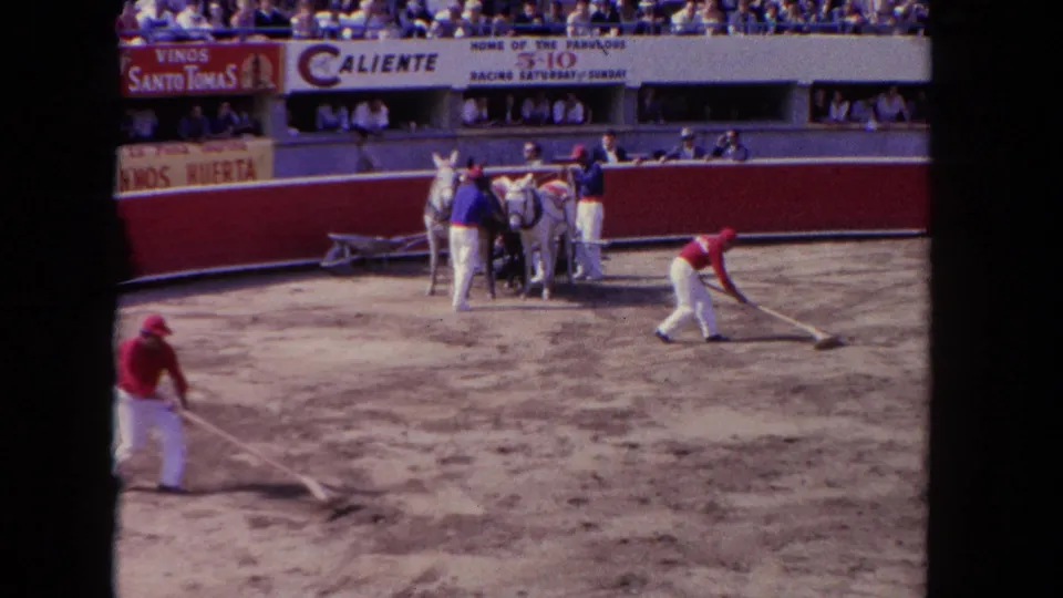 A 1962 Los Angeles racetrack view shows workers cleaning the ring while horses and handlers wait below crowded stands.