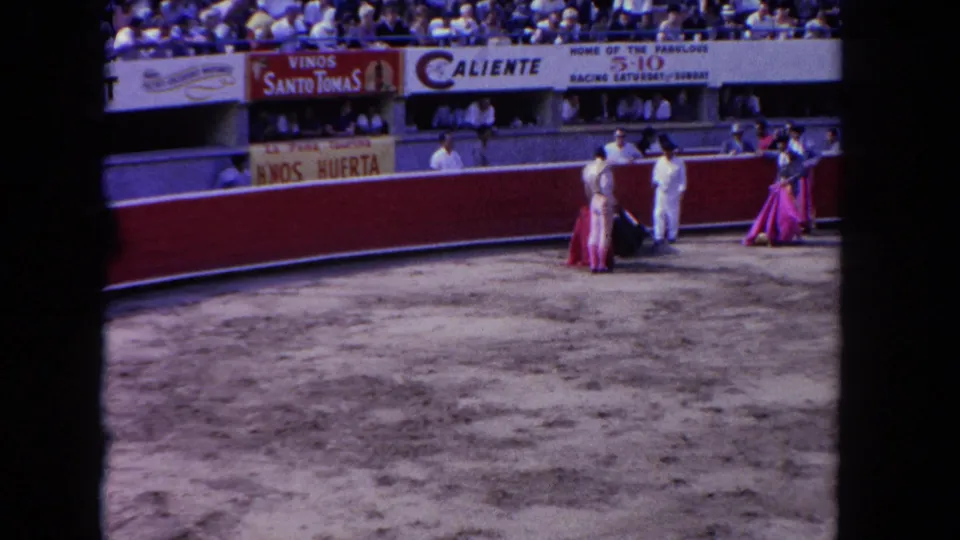 Wide 8mm view of a 1962 Los Angeles bullfighting-style arena event with attendants, matador figures, spectators, and visible signage.