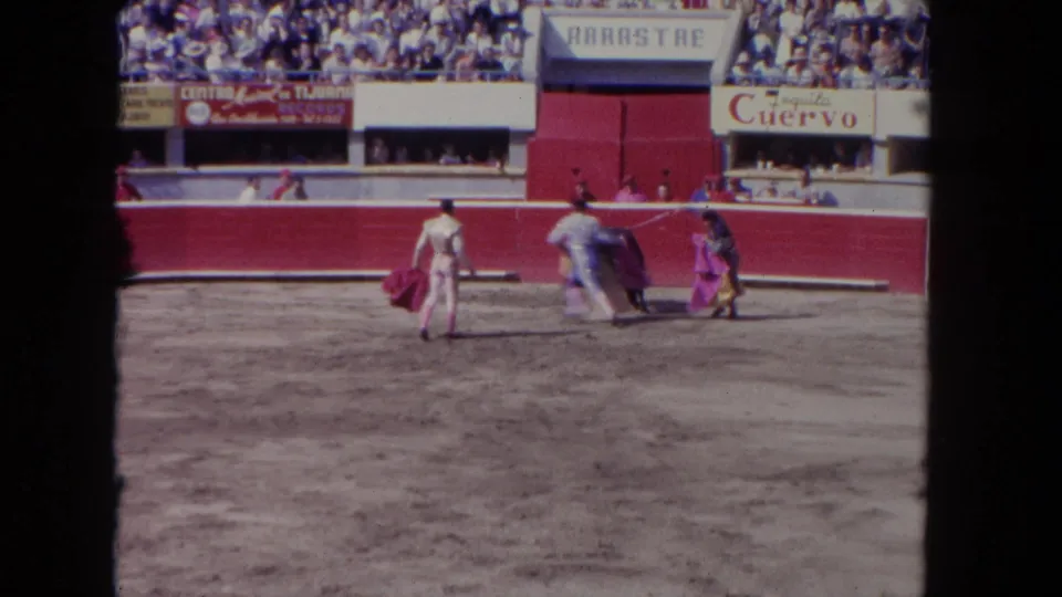 1962 Los Angeles 8mm frame with three matadors maneuvering capes near a black bull before a seated crowd.