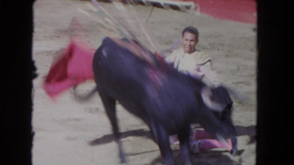 1962 Los Angeles 8mm frame with a black bull moving past a matador and red cape during an arena performance.