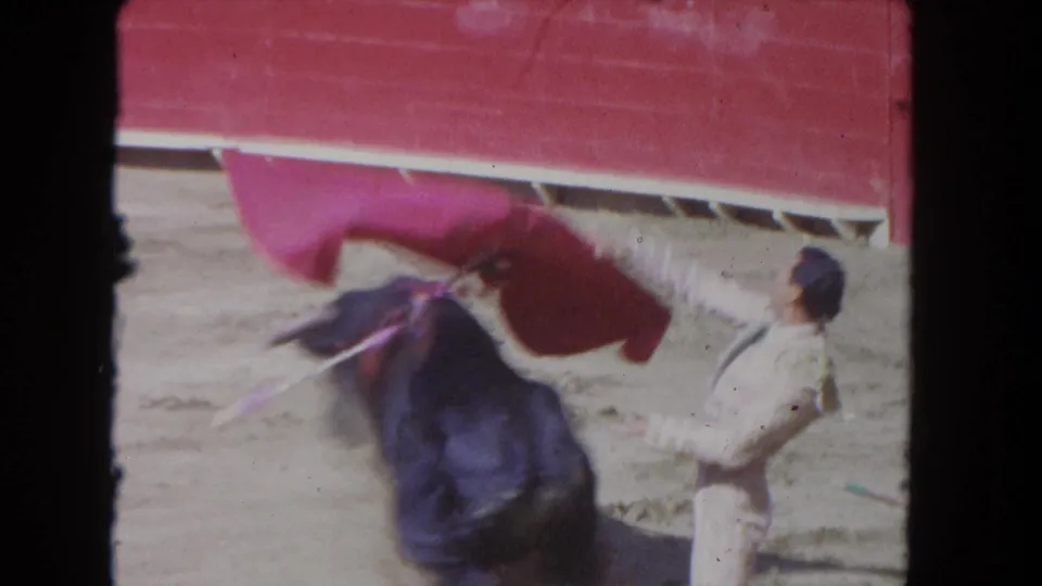 1962 Los Angeles 8mm frame showing the red cape raised above a black bull as the matador stands nearby.