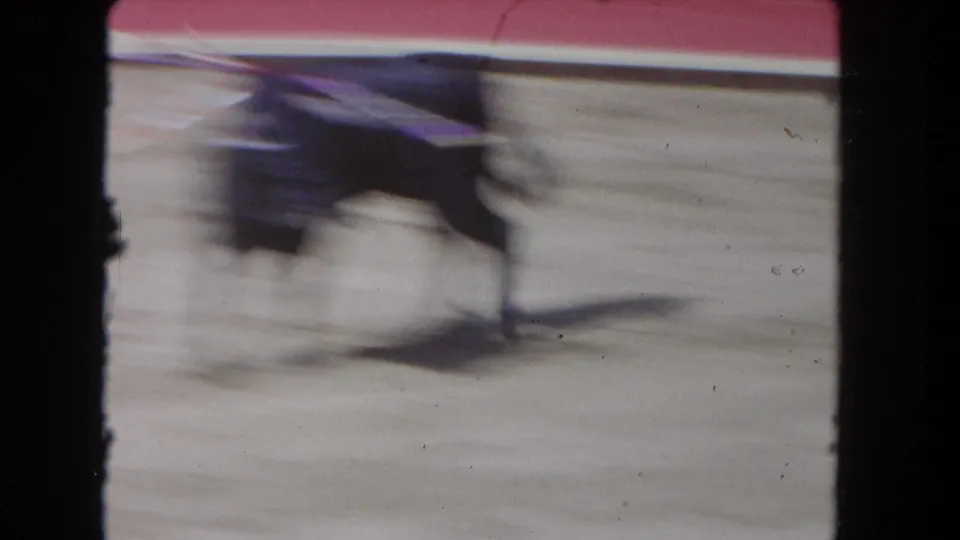 1962 Los Angeles 8mm frame with a motion-blurred black bull running across the arena near the red barrier.