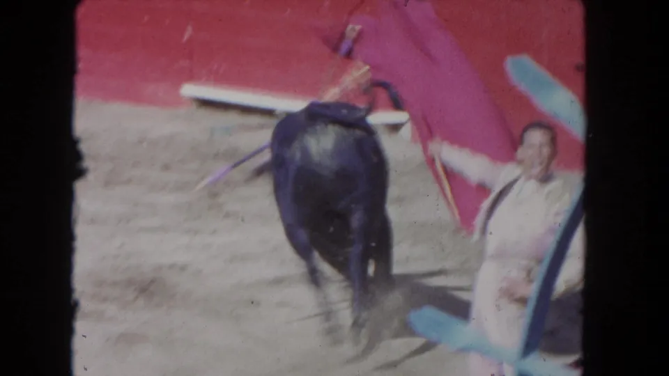 1960s 8mm frame appears to show a matador close to a dark bull beside a red cape in a sandy arena.