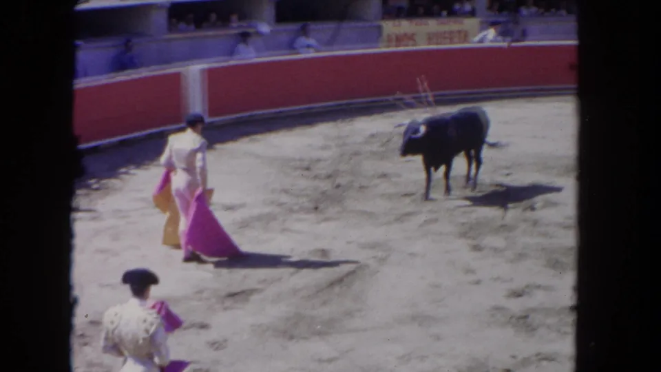 A matador holding a pink cape faces a black bull in a 1962 Los Angeles arena, with another matador partly visible below.