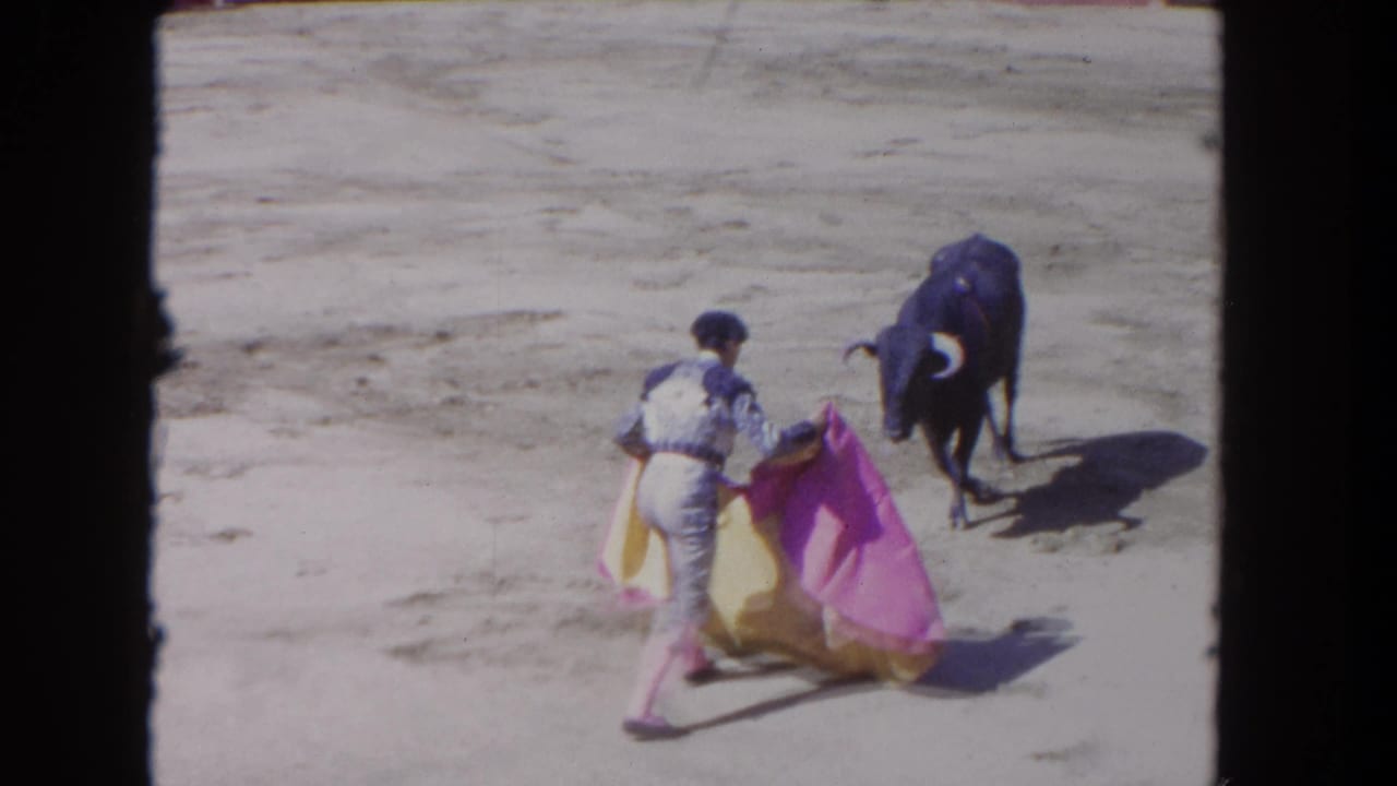 Matador in a bullring approaches a black bull with the cape spread, seen in soft 1962-era 8mm color.
