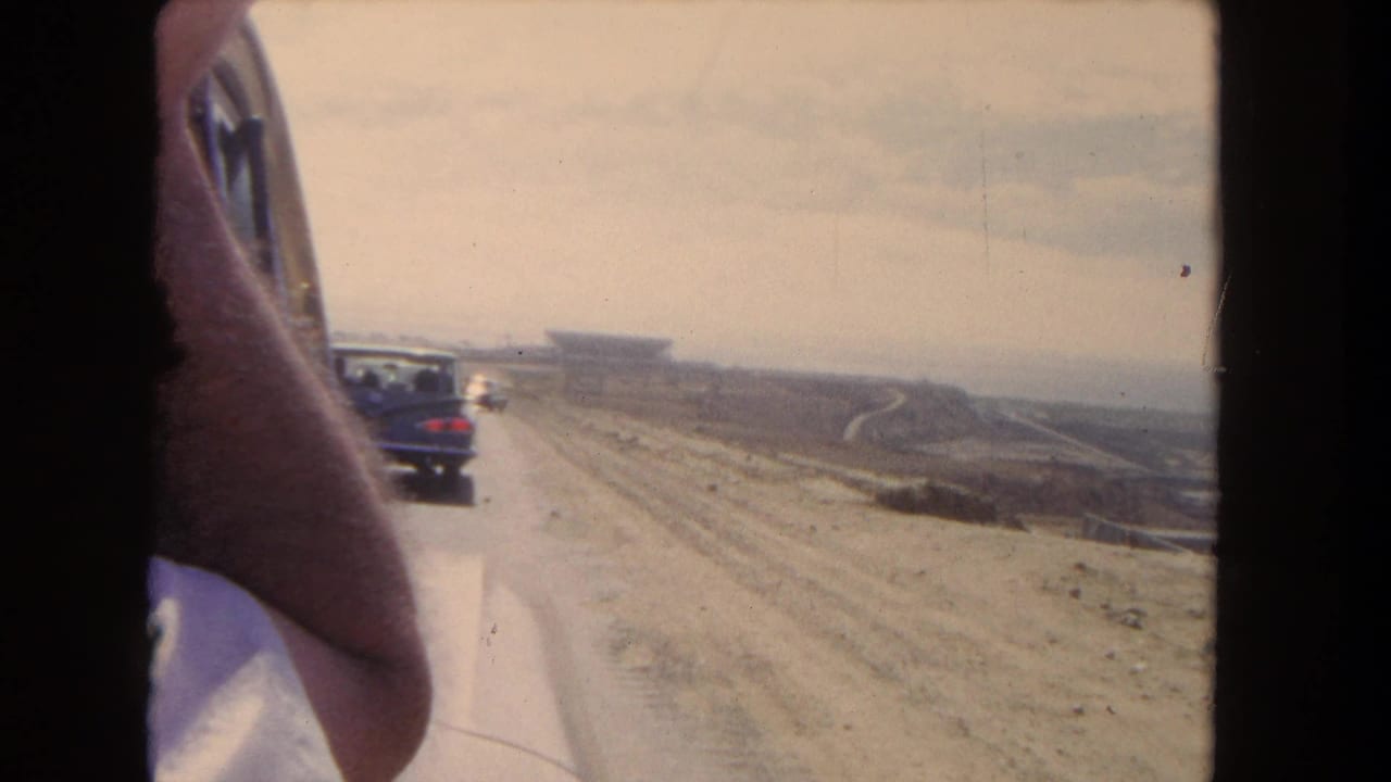 Passenger-window view of cars on a dusty highway with a distant large structure on the horizon.