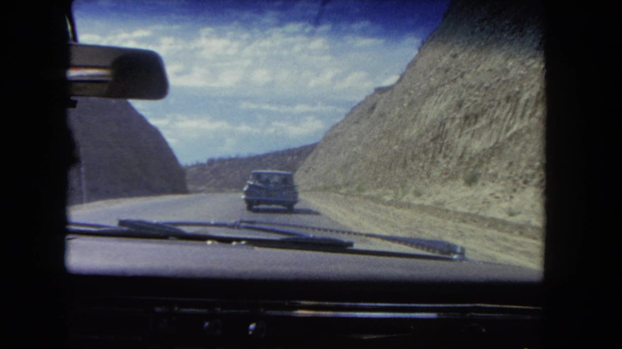 Dashboard perspective from 1962 home-movie footage showing a sedan ahead on a curving mountain road in Los Angeles County metadata context.