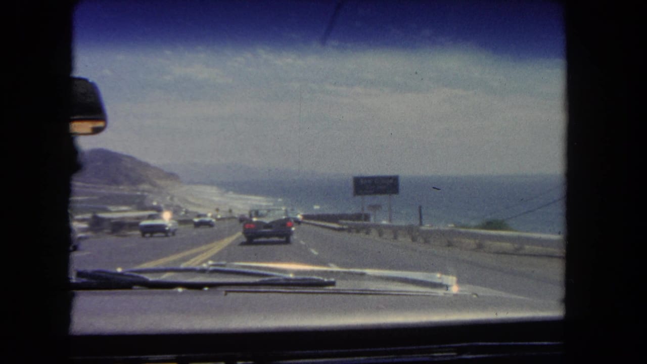 Coastal highway seen through a car windshield with traffic ahead and ocean at right.