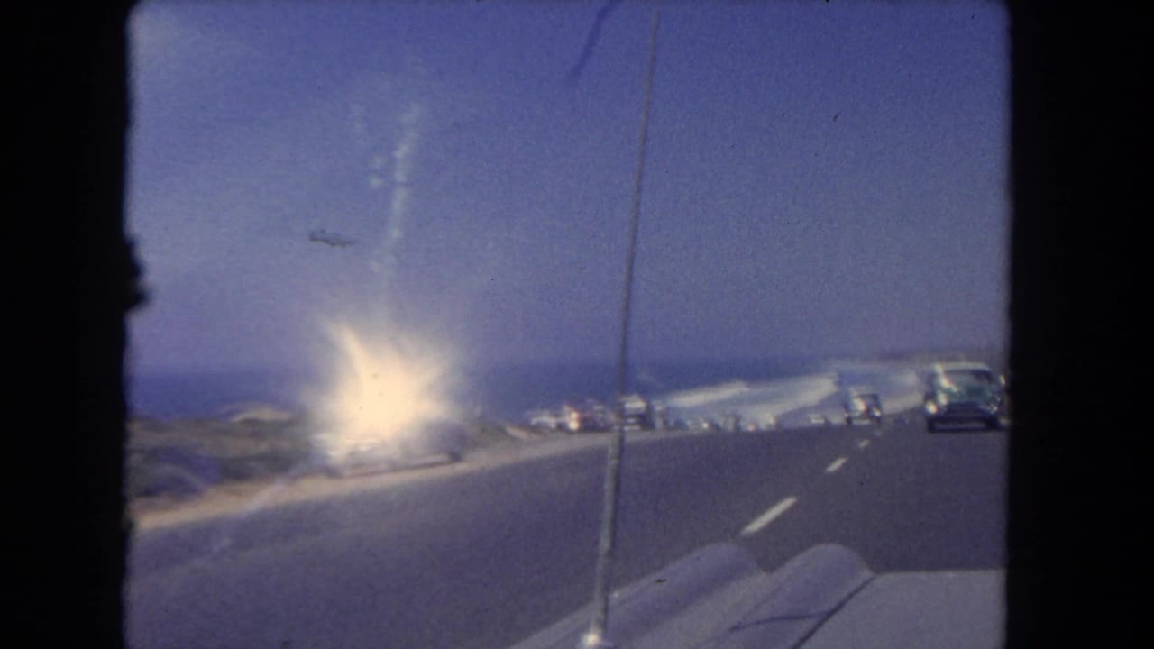 1962 Los Angeles-area coastal road viewed from inside a moving car, with surf, roadway, and early-1960s cars visible.
