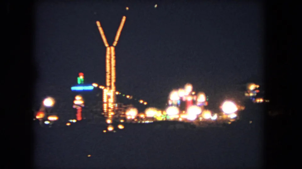 1962 Los Angeles home-movie frame showing distant carnival lights and a tall illuminated ride structure at night.