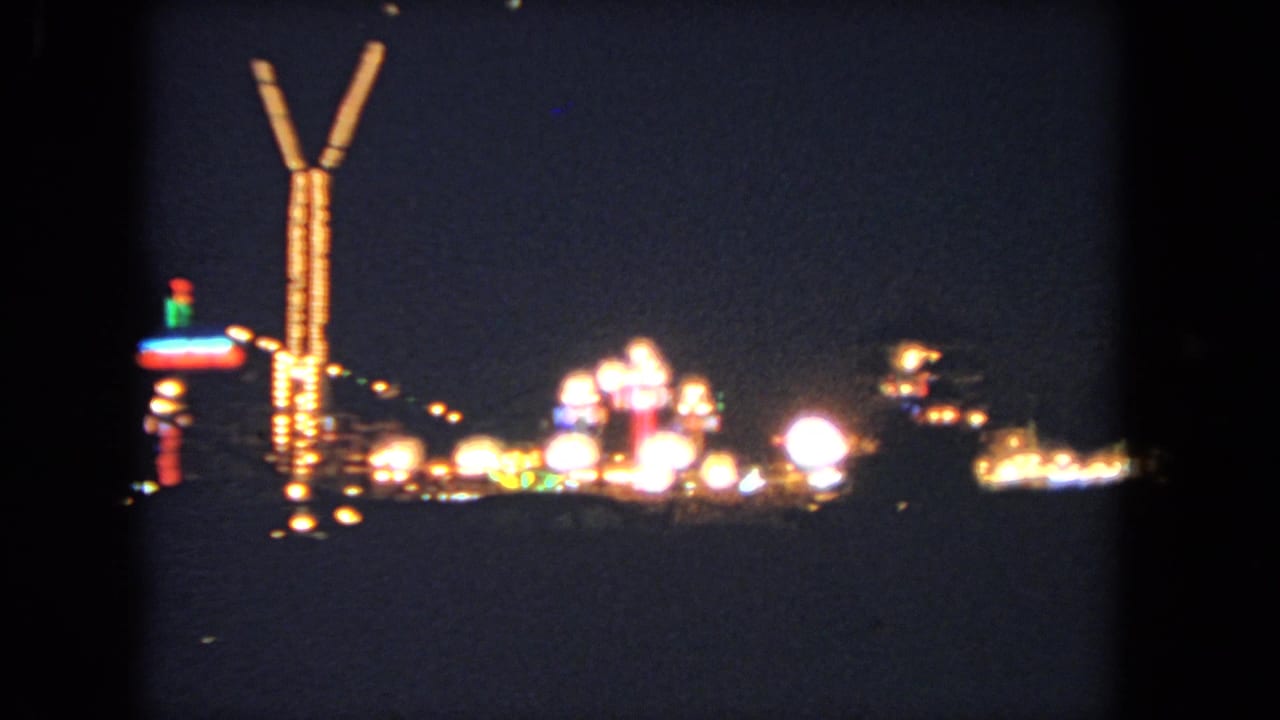 Distant nighttime midway lights with a tall glowing ride structure near the center.