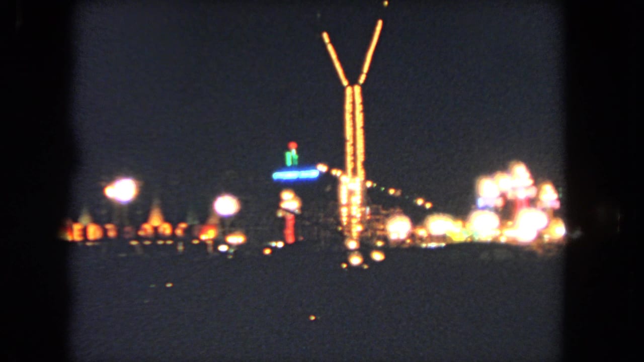 Soft-focus night view of a tall Y-shaped light structure and glowing rides.