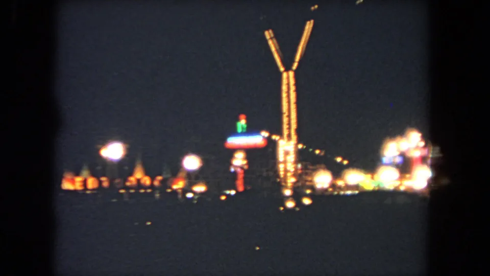 1962 Los Angeles 8mm frame showing the illuminated Y-shaped ride structure beside glowing fairground attractions.