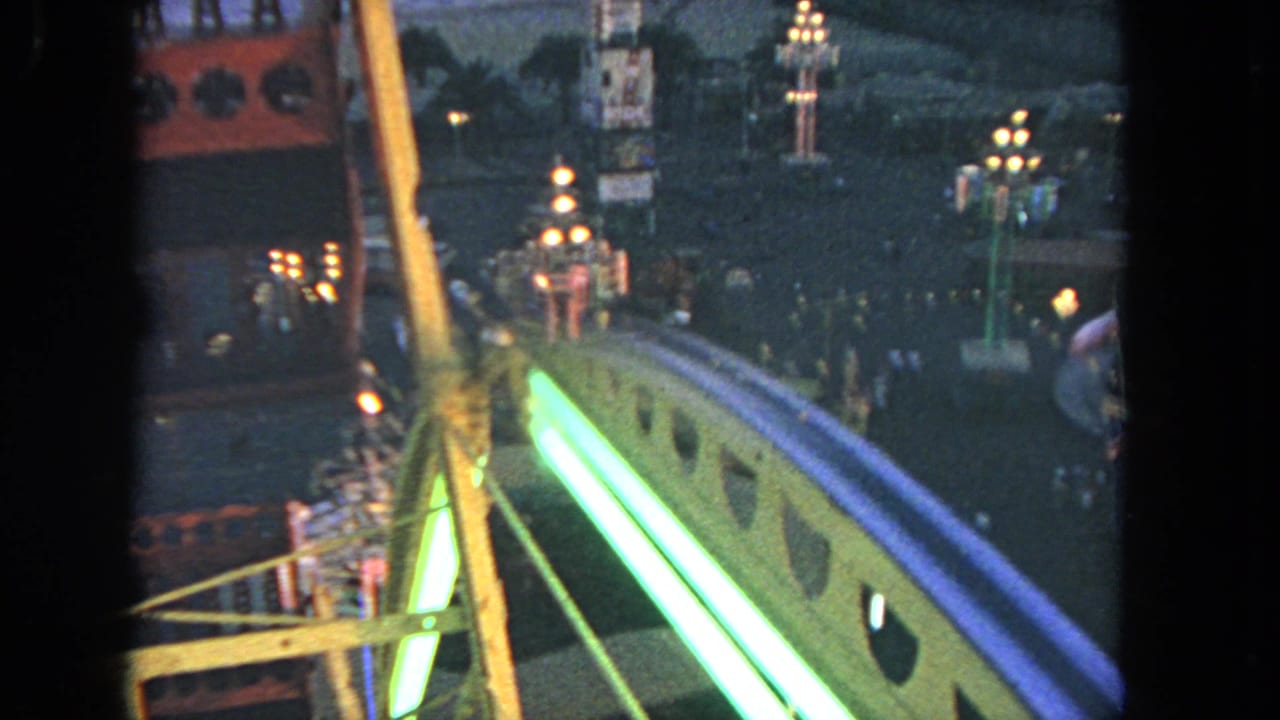 View from a Ferris wheel over a lit carnival ride and crowded fairground at dusk.