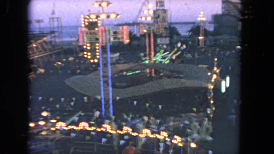 1962 Los Angeles fairground frame showing a bulb-lined midway, blue light columns, palm plantings, and small figures moving below.