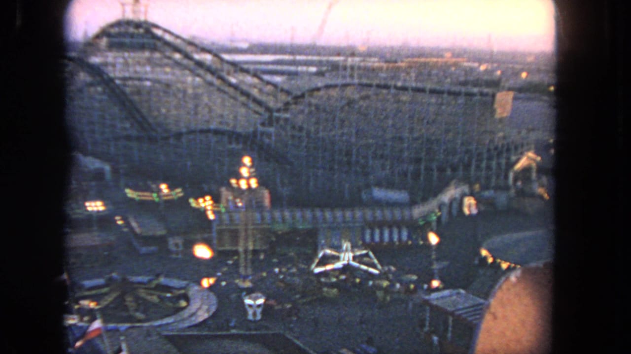Elevated 1962 Los Angeles home-movie view of a wooden roller coaster and lit midway attractions during dusk.