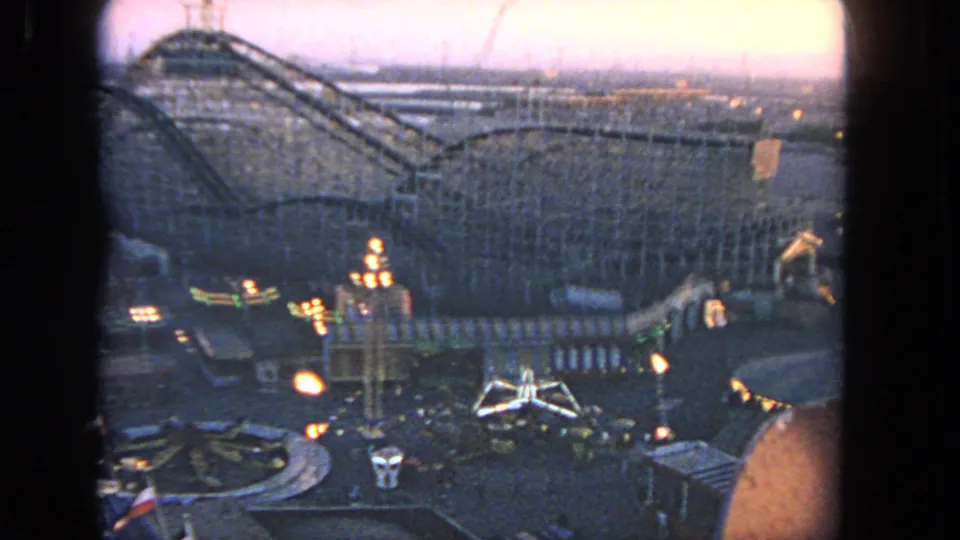 Elevated 1962 Los Angeles home-movie view of a wooden roller coaster and lit midway attractions during dusk.