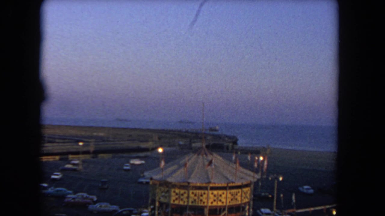 Dusk view of a carousel roof, parked cars, seawall, and ocean horizon.