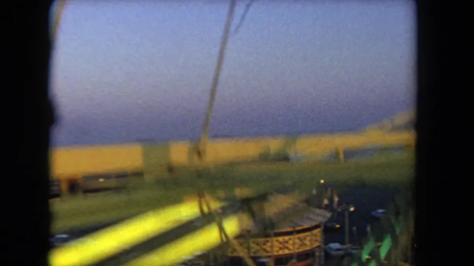 Moving Ferris wheel view over a carousel area near the ocean, with motion blur and dusk color shifts.