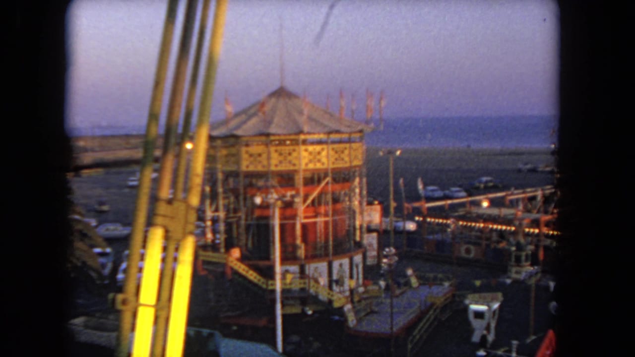Elevated view of a domed carnival ride structure with lights and parked cars beyond.