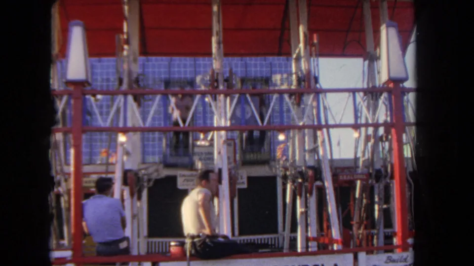 1962 Los Angeles amusement-park frame showing spectators below a red vertical ride as a cage passes through the structure.