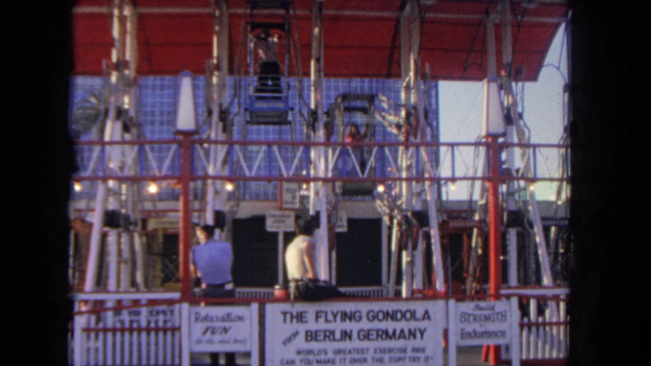 Flying Gondola ride structure with two men standing near signs at the base.