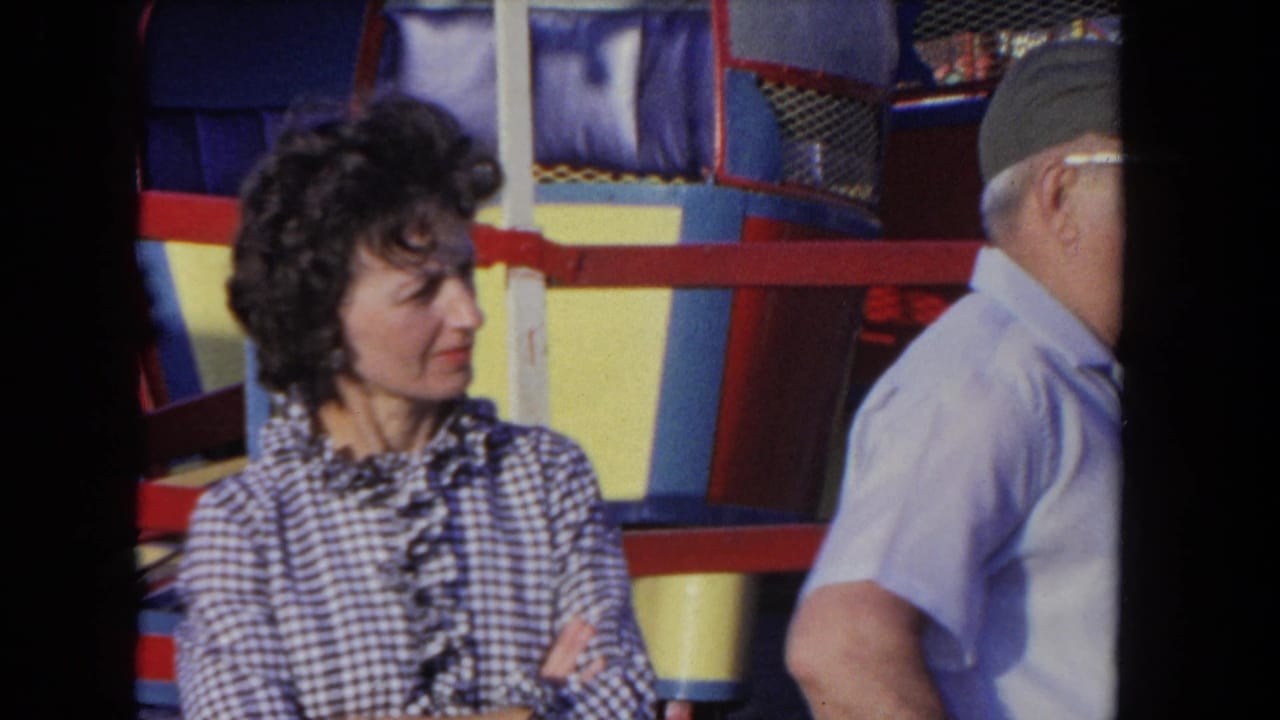 Woman near amusement ride panels as an older man passes at the edge of frame.