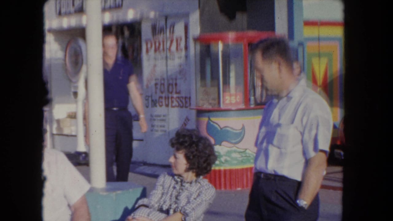 Three adults near a colorful carnival game booth with prize signage.