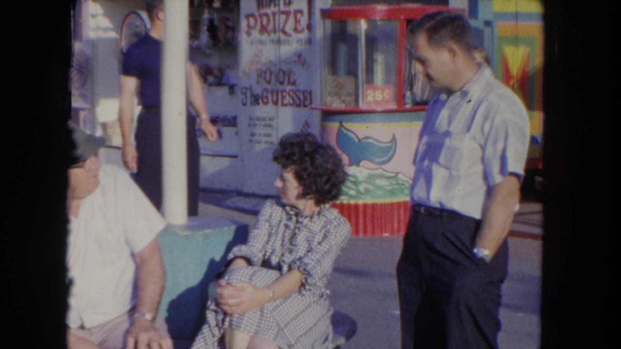 Adults seated and standing beside a carnival booth with a red-framed game window.