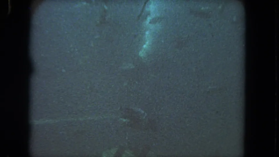1962 Los Angeles 8mm frame with dim underwater visibility, dark vertical film edges, grain, scratches, and pale indistinct shapes near the top.