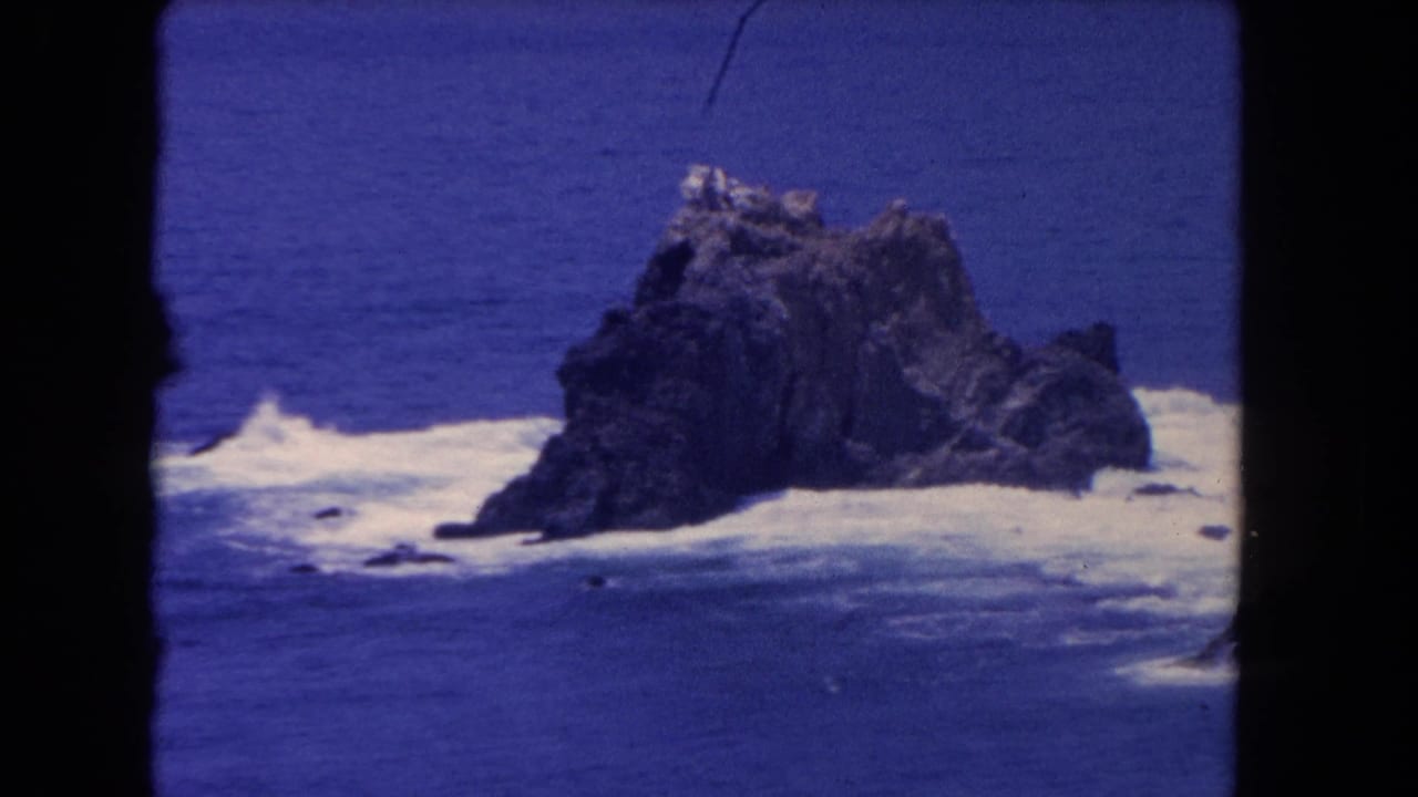 1962 Los Angeles-area 8mm frame showing a large offshore rock with waves breaking around it in deep blue water.