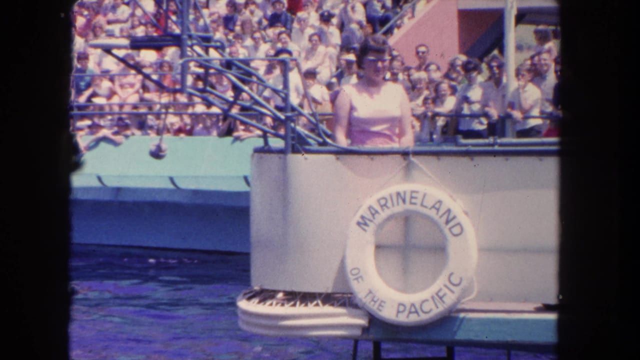 Woman at a show platform with Marineland of the Pacific life-ring sign and spectators behind.