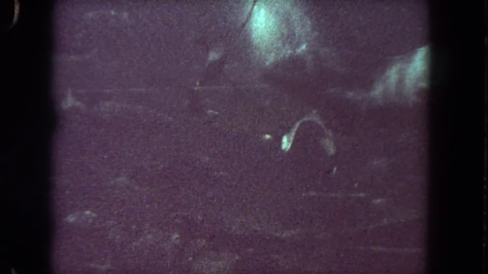 1962 Los Angeles-area 8mm frame showing a dark underwater diver shape with pale highlights, scratches, and dense grain.