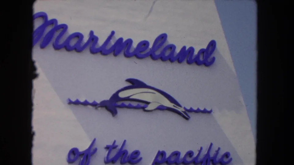Visitor-shot 8mm frame of the Marineland sign, showing the name, dolphin emblem, and partial phrase "of the pacific."