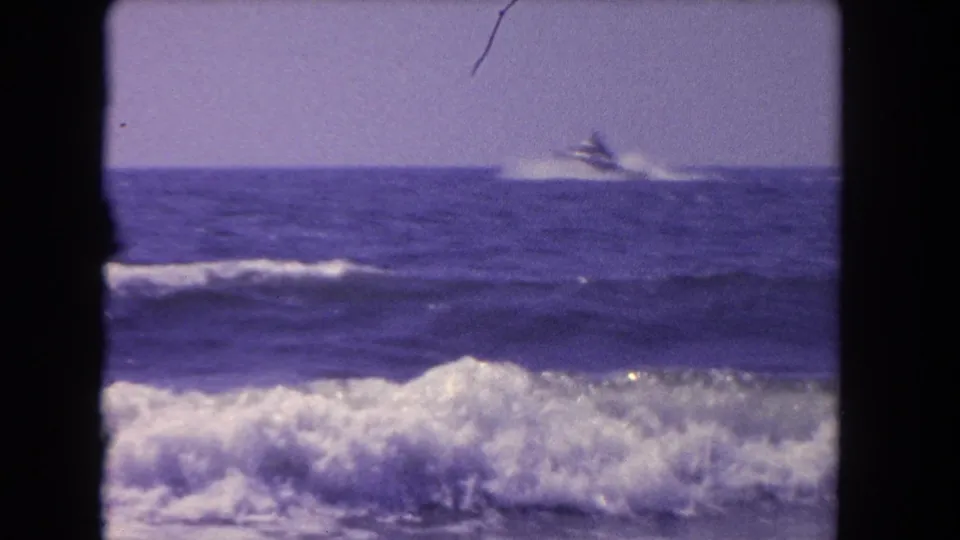 A distant speedboat appears over ocean swell in 1962 Los Angeles coastal home-movie footage, framed by breaking waves.
