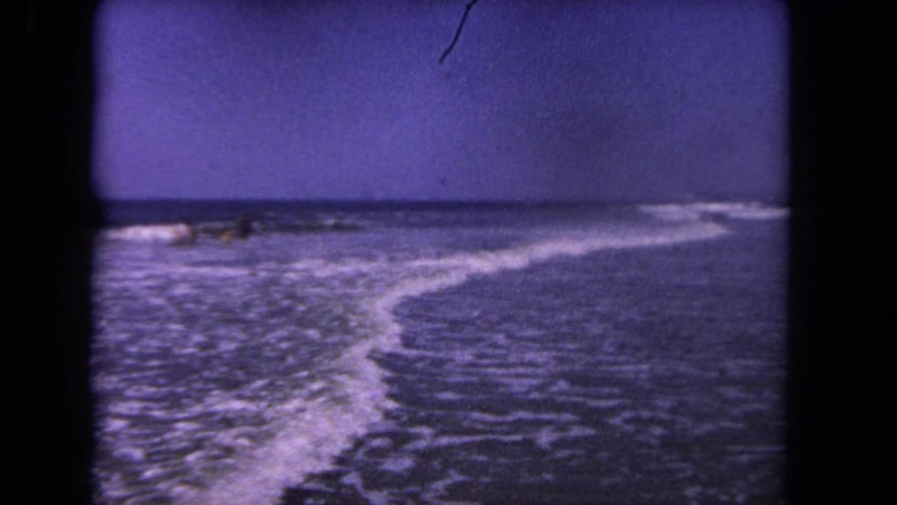 Breaking surf along a beach with small distant figures near the waterline.