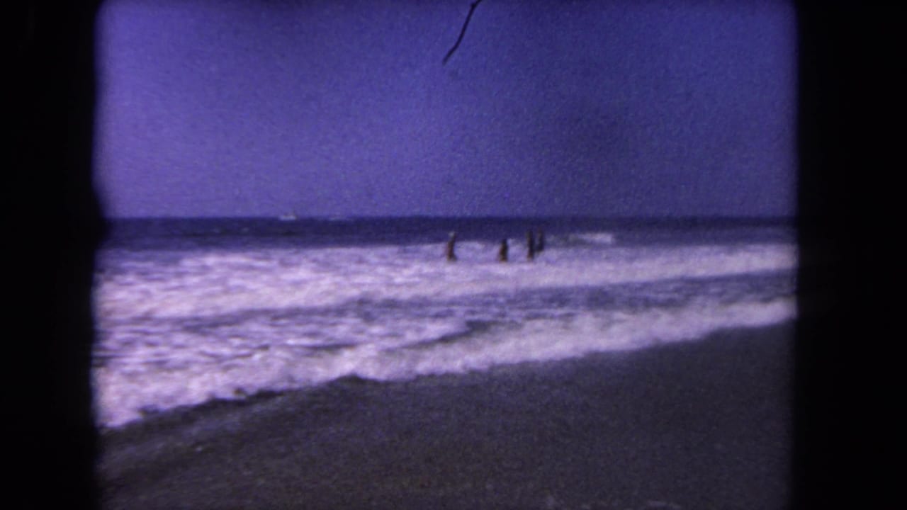 Distant people wade in ocean surf under a dark purple-blue sky.