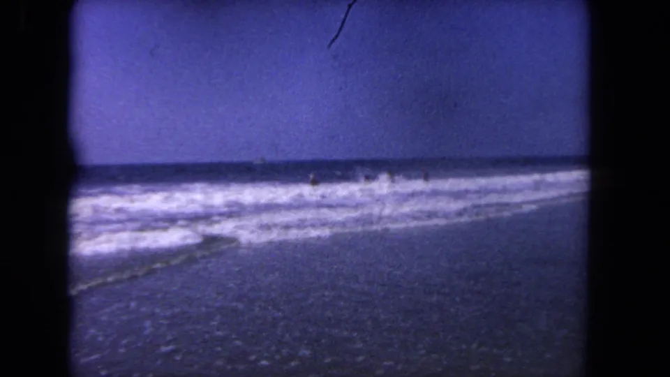 1962 Los Angeles home-movie view of foamy ocean waves washing over wet beach beneath a blue sky.