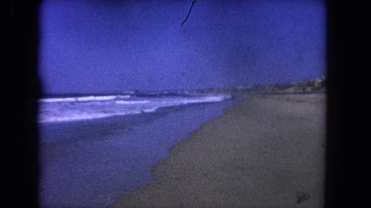 Blue sky over low waves washing onto a sandy beach with dark film borders.