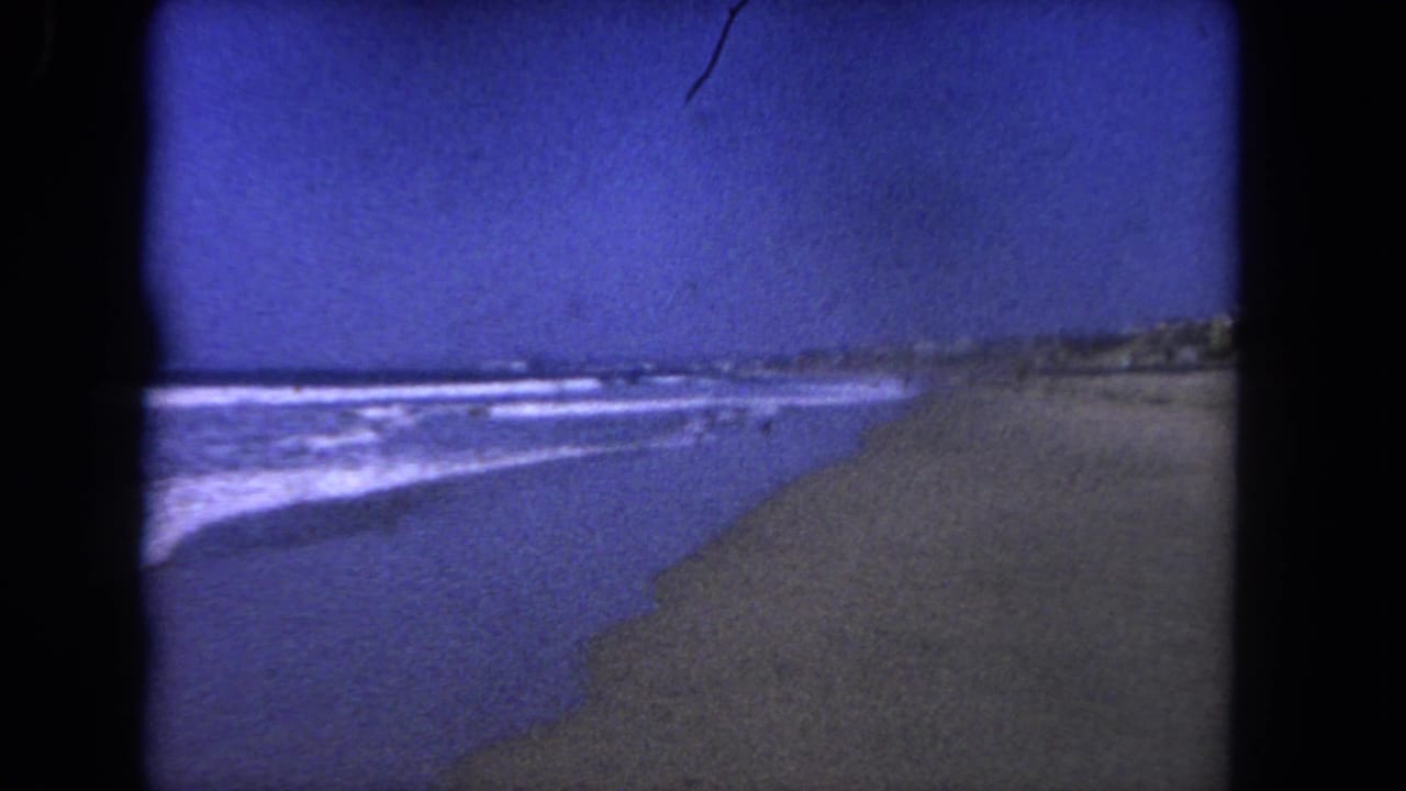 Vintage 8mm view of waves lapping a Los Angeles-area beach, with distant shore detail and visible film grain.