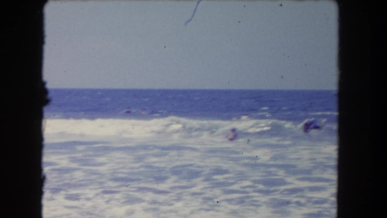 1962 Los Angeles beach scene with swimmers partly obscured by breaking waves and open water beyond.