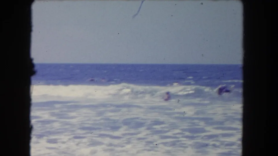 1962 Los Angeles beach scene with swimmers partly obscured by breaking waves and open water beyond.