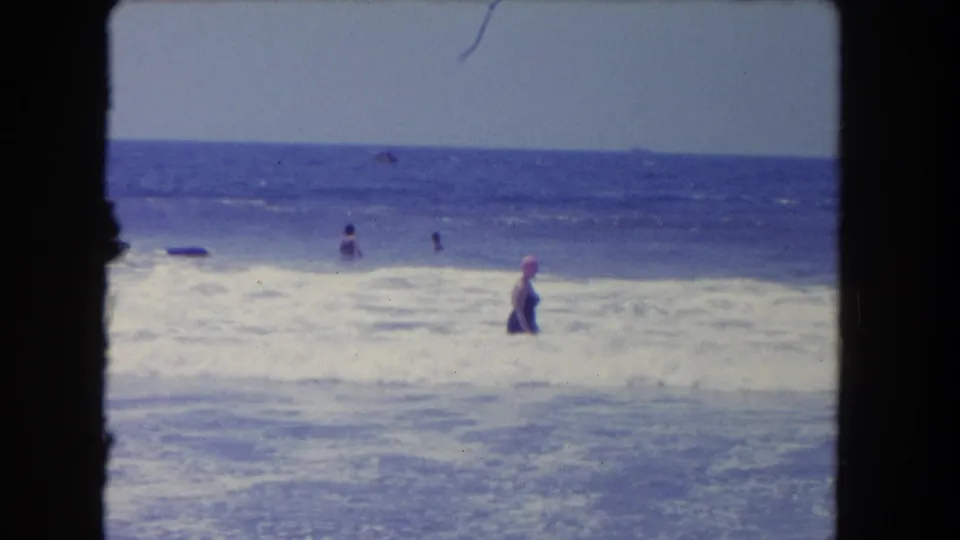 1962 Los Angeles-area beach footage showing a swimmer wading in white surf with several distant bathers farther offshore.