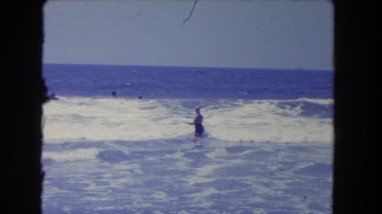Woman stands in foamy ocean water while distant swimmers face the surf.