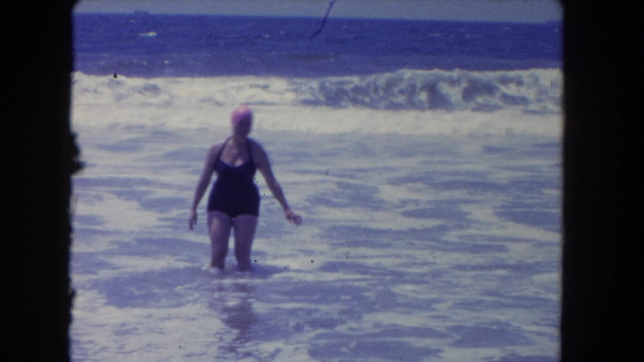 Adult woman in swimwear wades through foamy Pacific surf at a Los Angeles beach in metadata-dated 1962 footage.