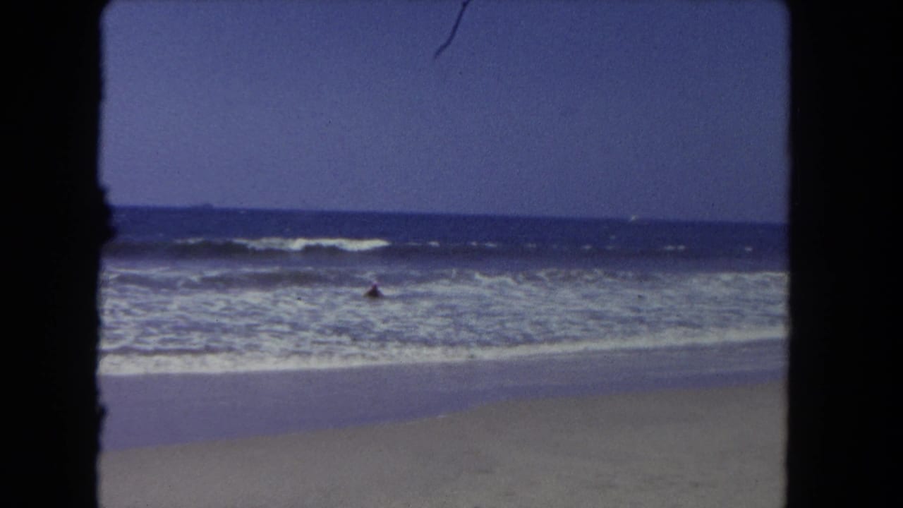 Wide beach view with ocean waves, wet sand, blue sky, and dark film borders.