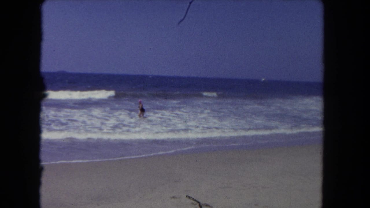Distant person in surf with waves breaking along a sandy beach.