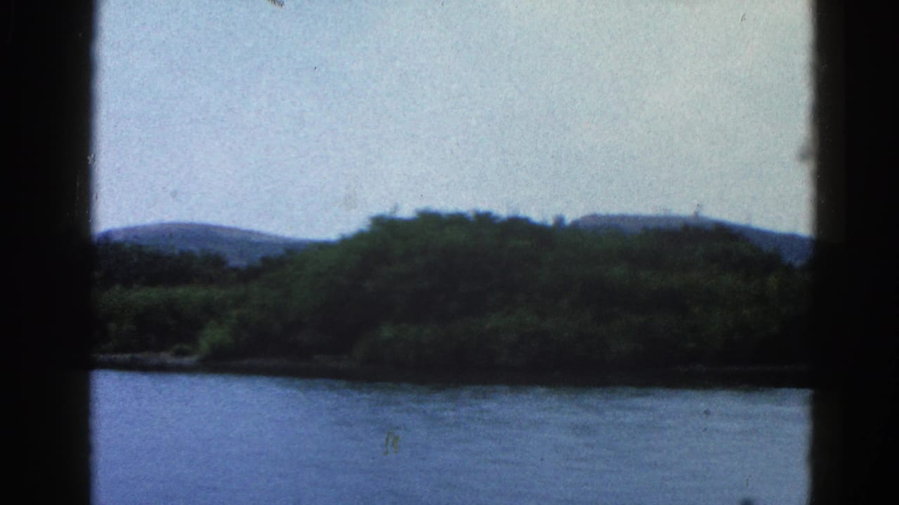 8mm home movie frame, circa 1962 Illinois — wide river with green far bank and low rolling hills, shot from aboard a moving boat.