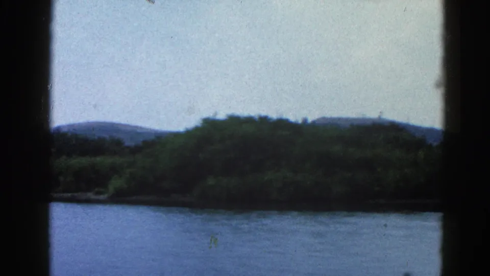 8mm home movie frame, circa 1962 Illinois — wide river with green far bank and low rolling hills, shot from aboard a moving boat.